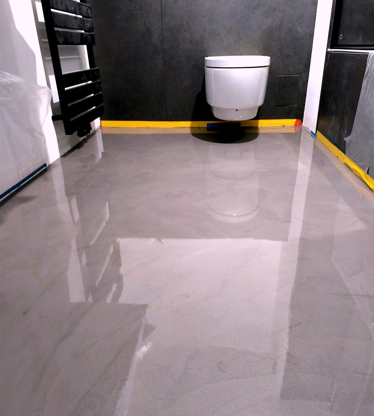 Fugenloser PU-Boden im Badezimmer vor einer dunklen Wandfläche, kurz vor der Mattversiegelung